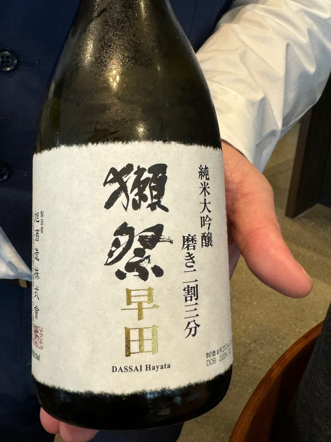 A hand holding a bottle of Dassai 23 from Yamaguchi, the label reading Hayata, junmai daiginjo polished to 23 per cent
