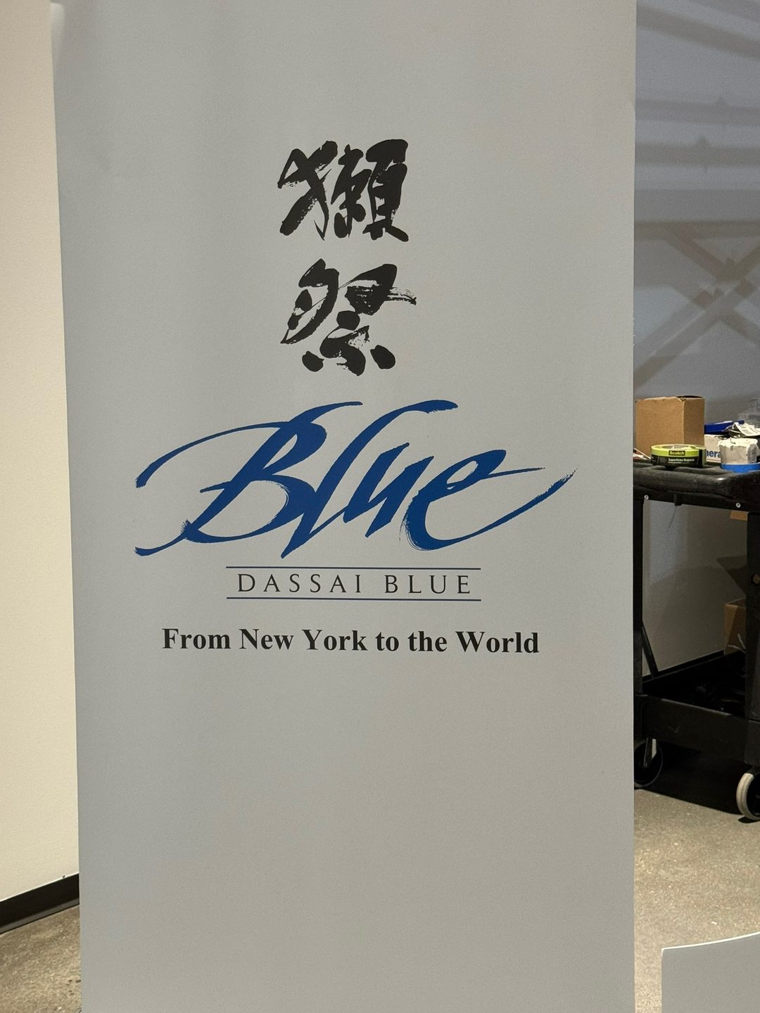 A white pillar sign at Dassai Blue carrying the brewery&rsquo;s logo and the words From New York to the World