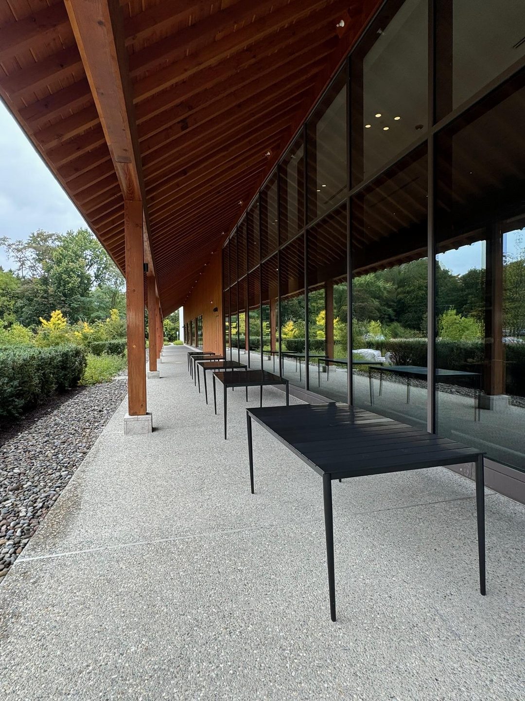 The deep timber eaves and full-height glass wall of Dassai Blue, with black tables on the terrace and garden planting in front