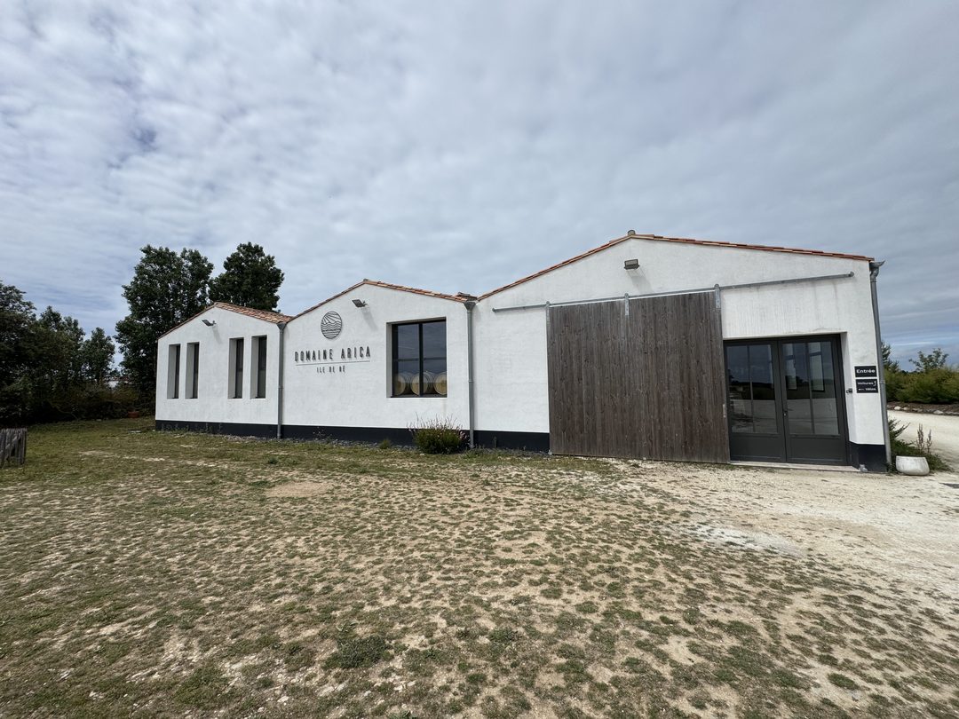 The white winery building of Domaine Arica, its name and circular wave logo painted on the wall