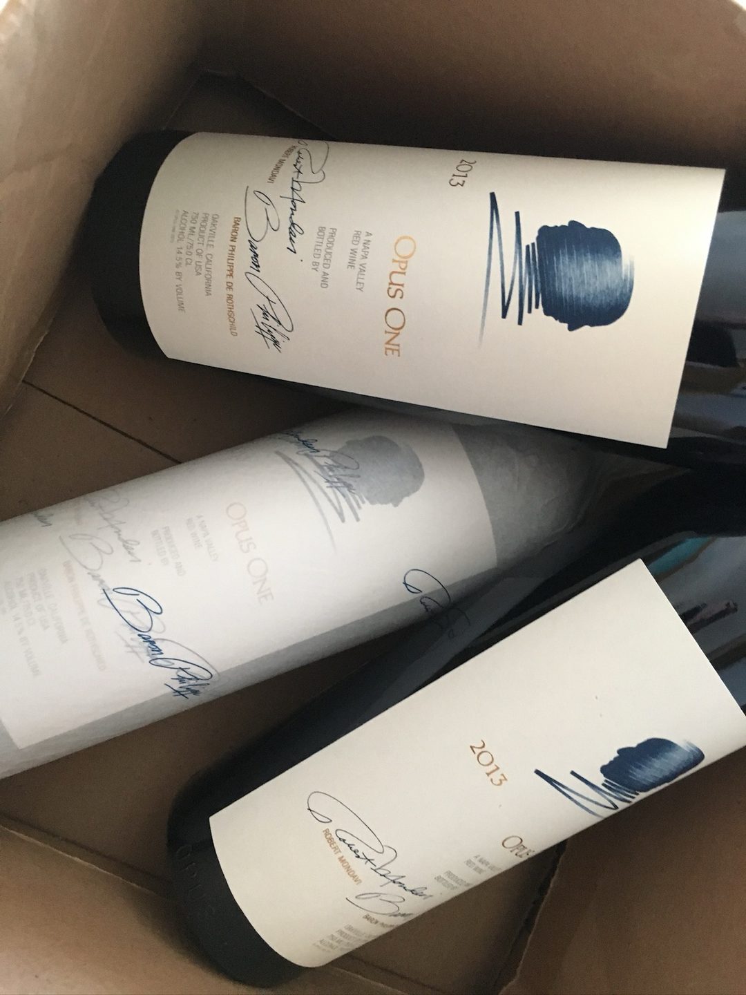 Three bottles of Opus One 2013 in their case at home, bound for the cellar, the labels showing the profiles of the two founders