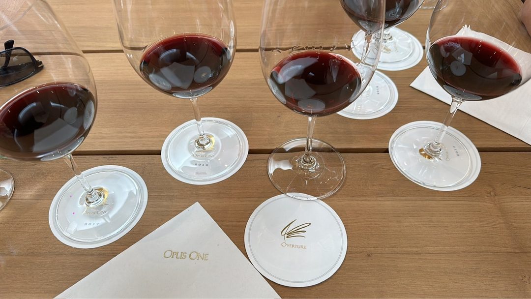 Glasses of Opus One and Overture poured on a wooden table at Opus One, on printed coasters