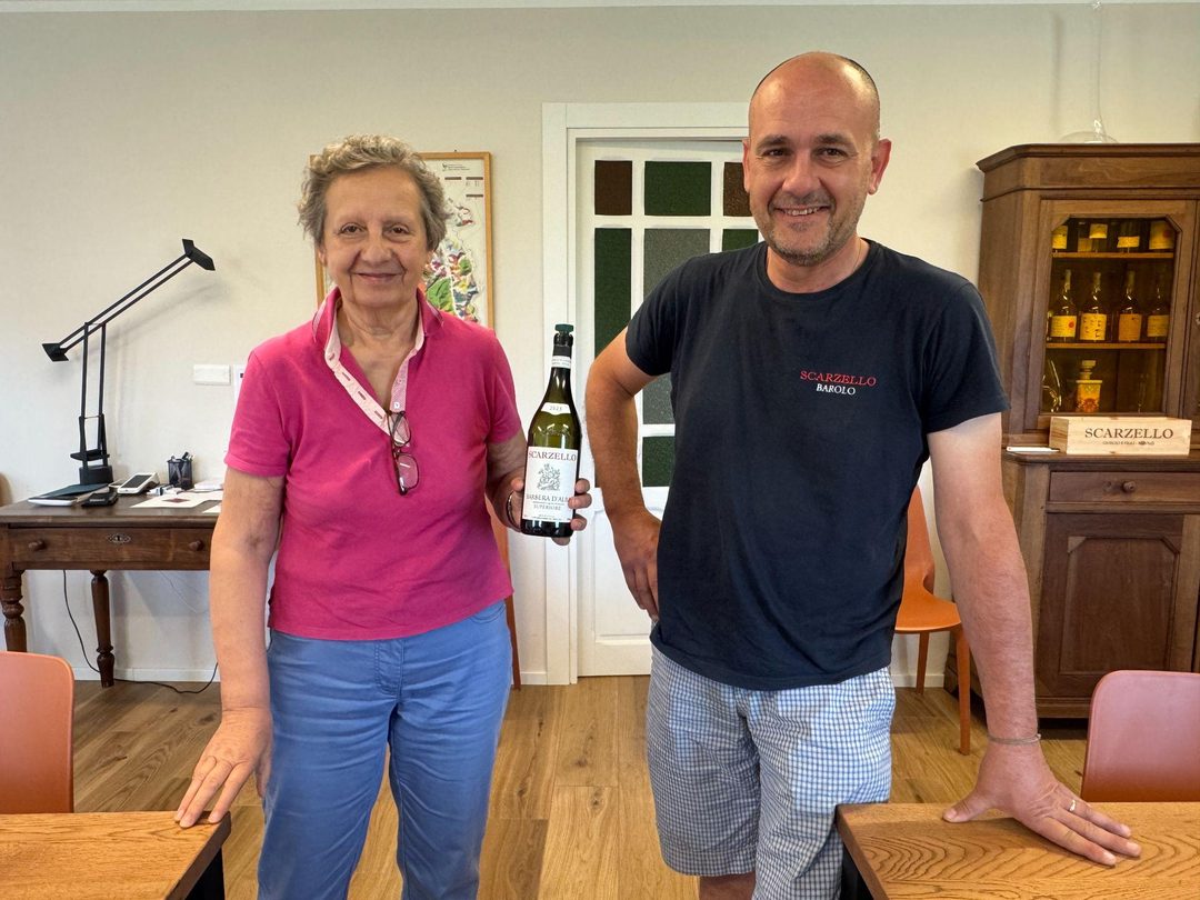 Gemma Scarzello holding a bottle of the estate&rsquo;s Barbera d&rsquo;Alba Superiore, standing with her son Federico in the tasting room