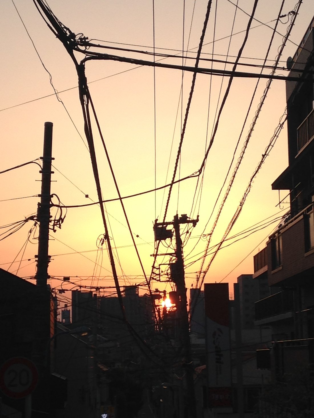 Utility poles and a dense tangle of wires silhouetted against an orange Tokyo sunset