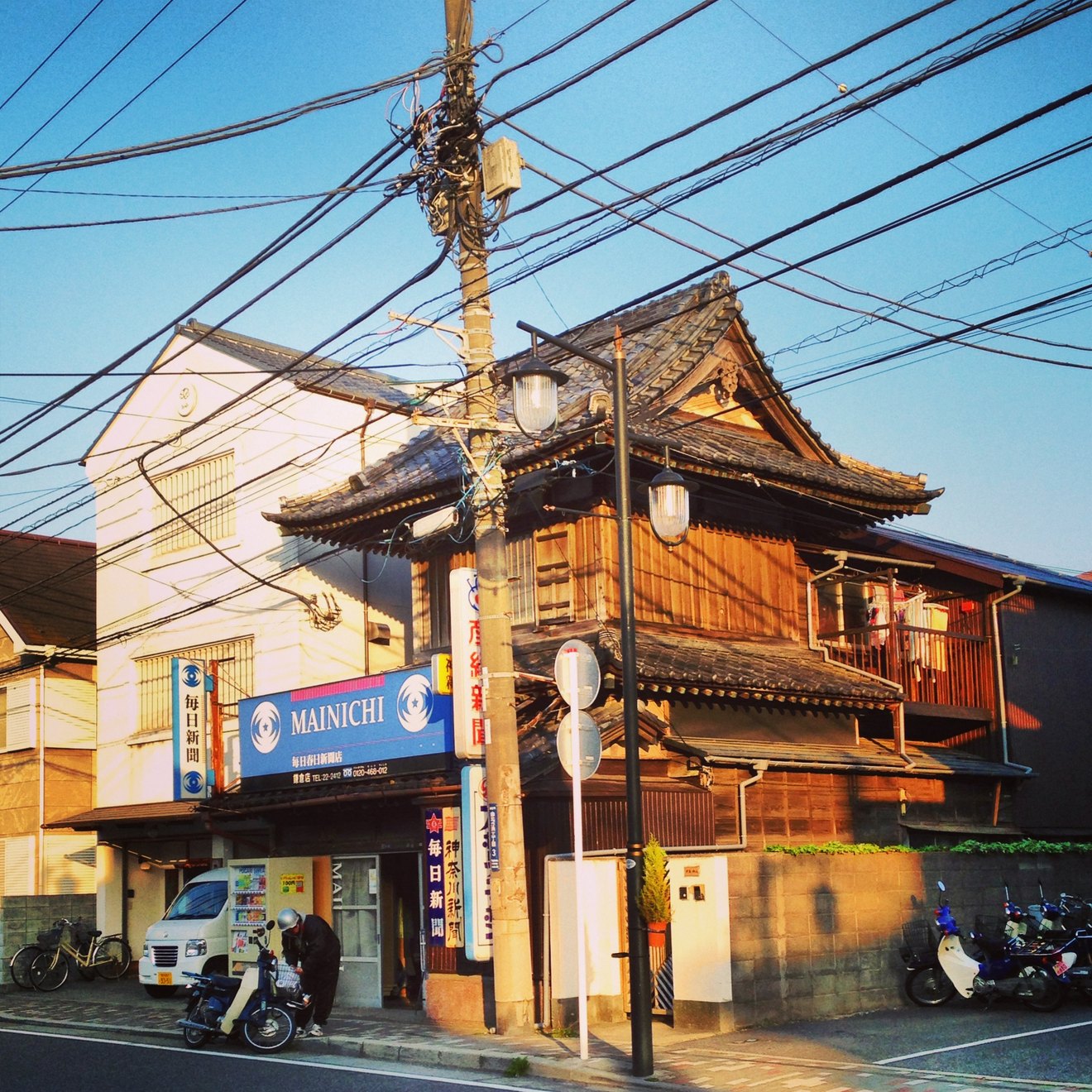 A traditional wooden Japanese house on a Tokyo street corner, a utility pole and dense wires in front of it